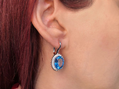 Diamond and oval blue topaz earrings in 14 carat white gold